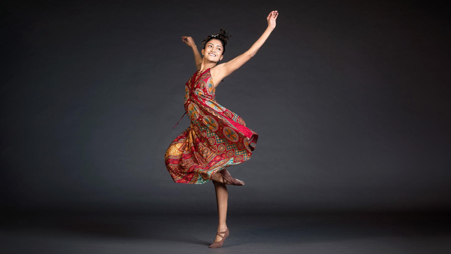Woman in red patterned dress spinning on one foot with her arms raised joyously.