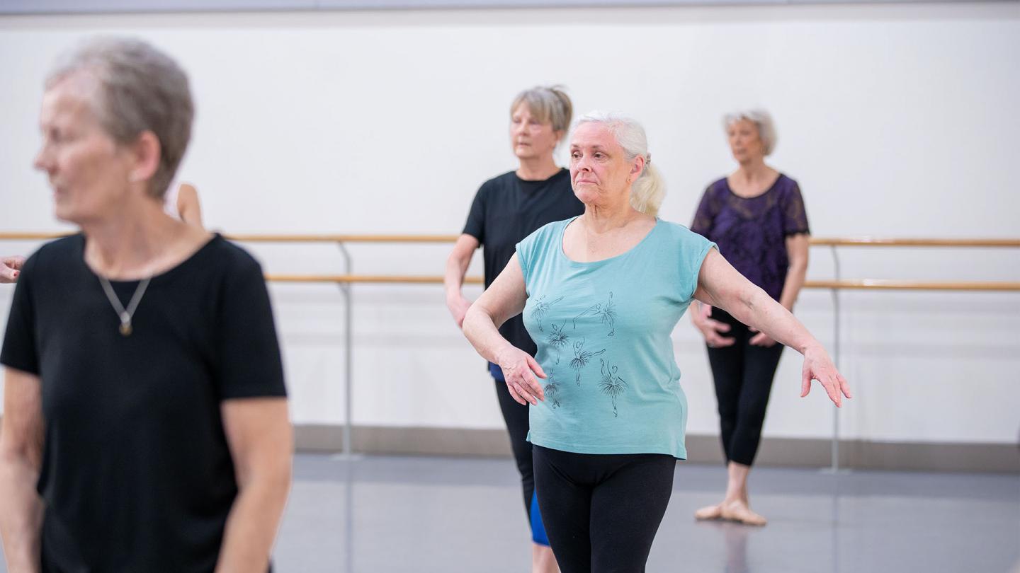 Silver-haired lady in turquoise T-shirt taking ballet class