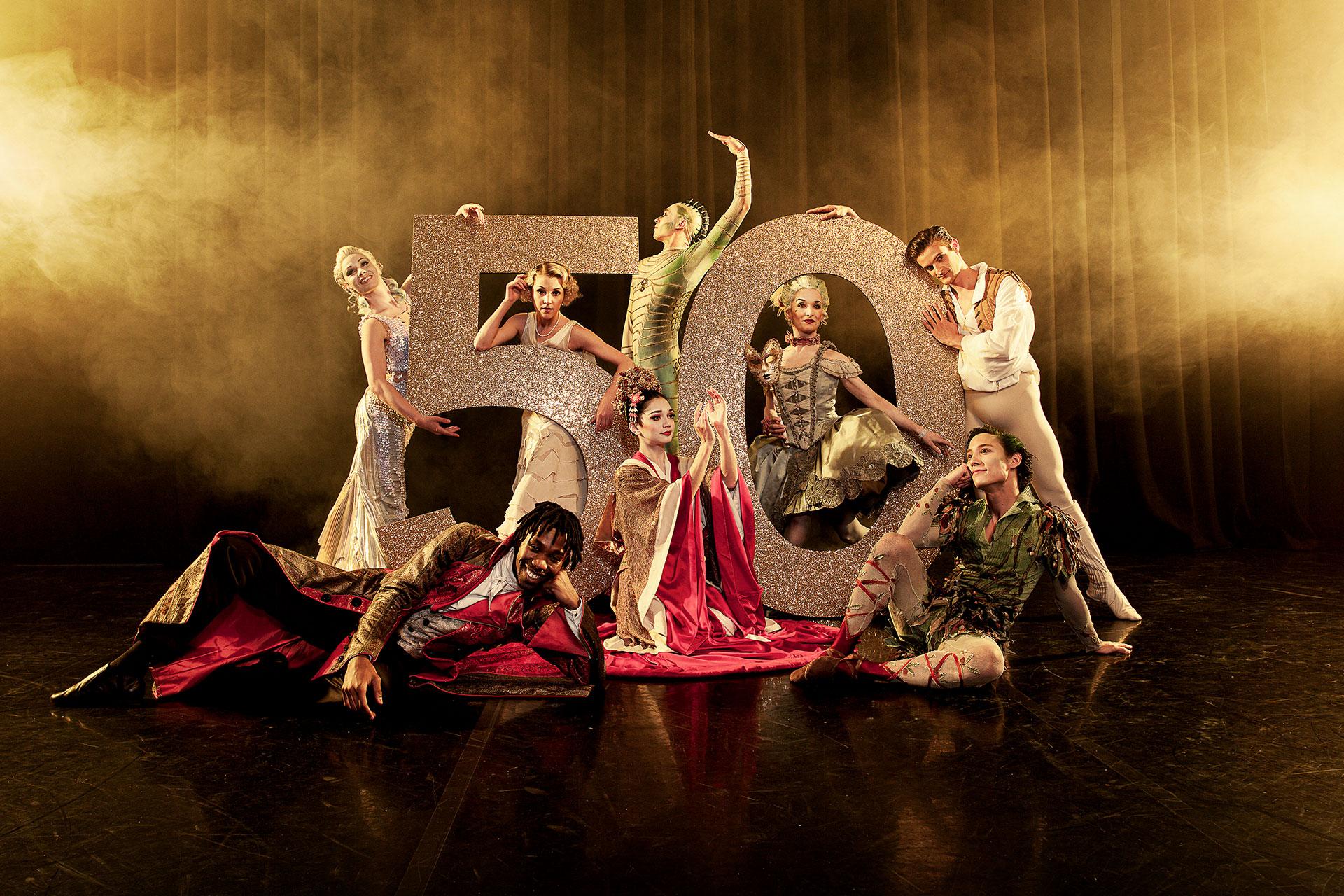 Northern Ballet dancers posing in front of a large number 50 wearing costumes of different productions. Photo Guy Farrow.