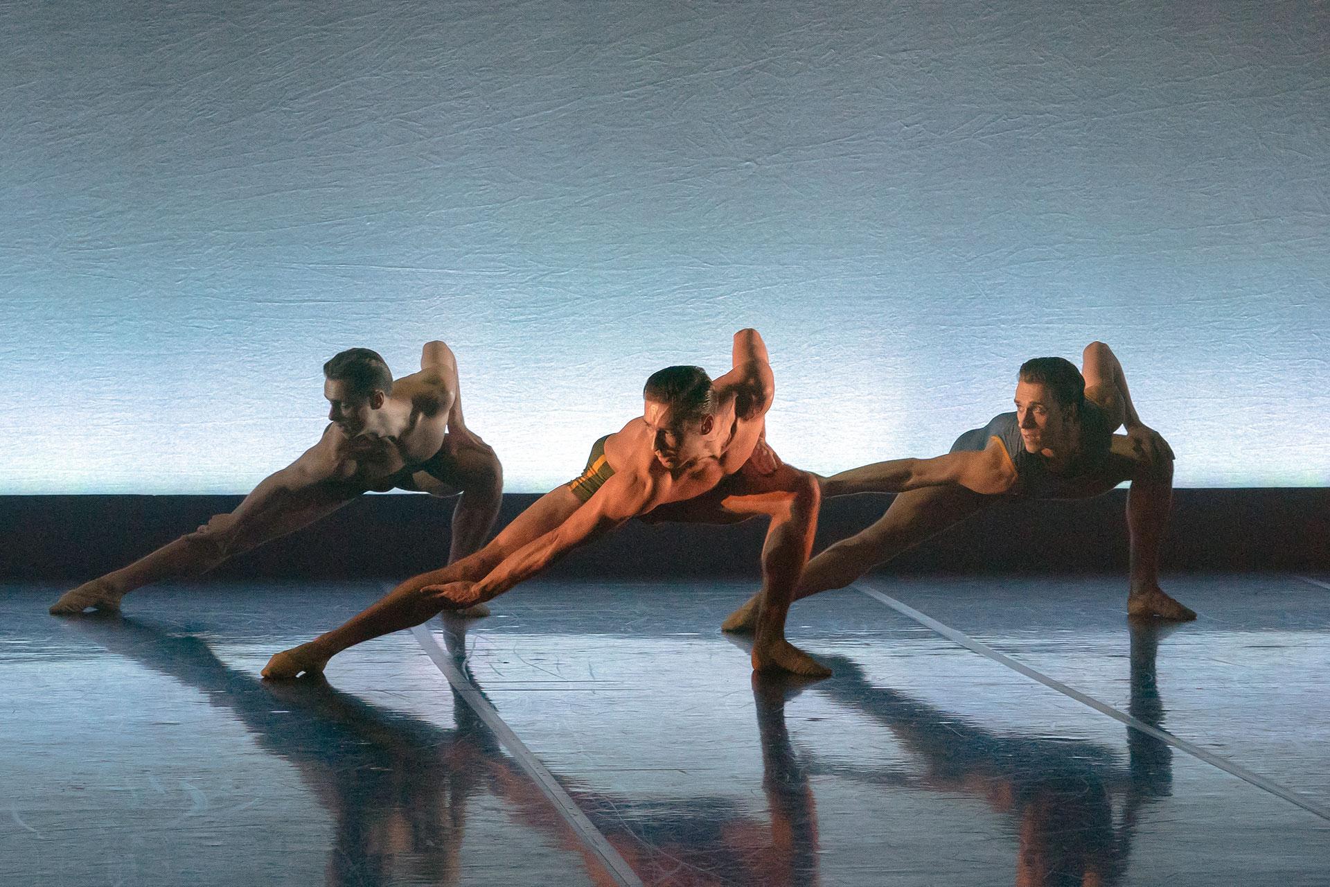 Three male dancers crouch with one leg stretched straight