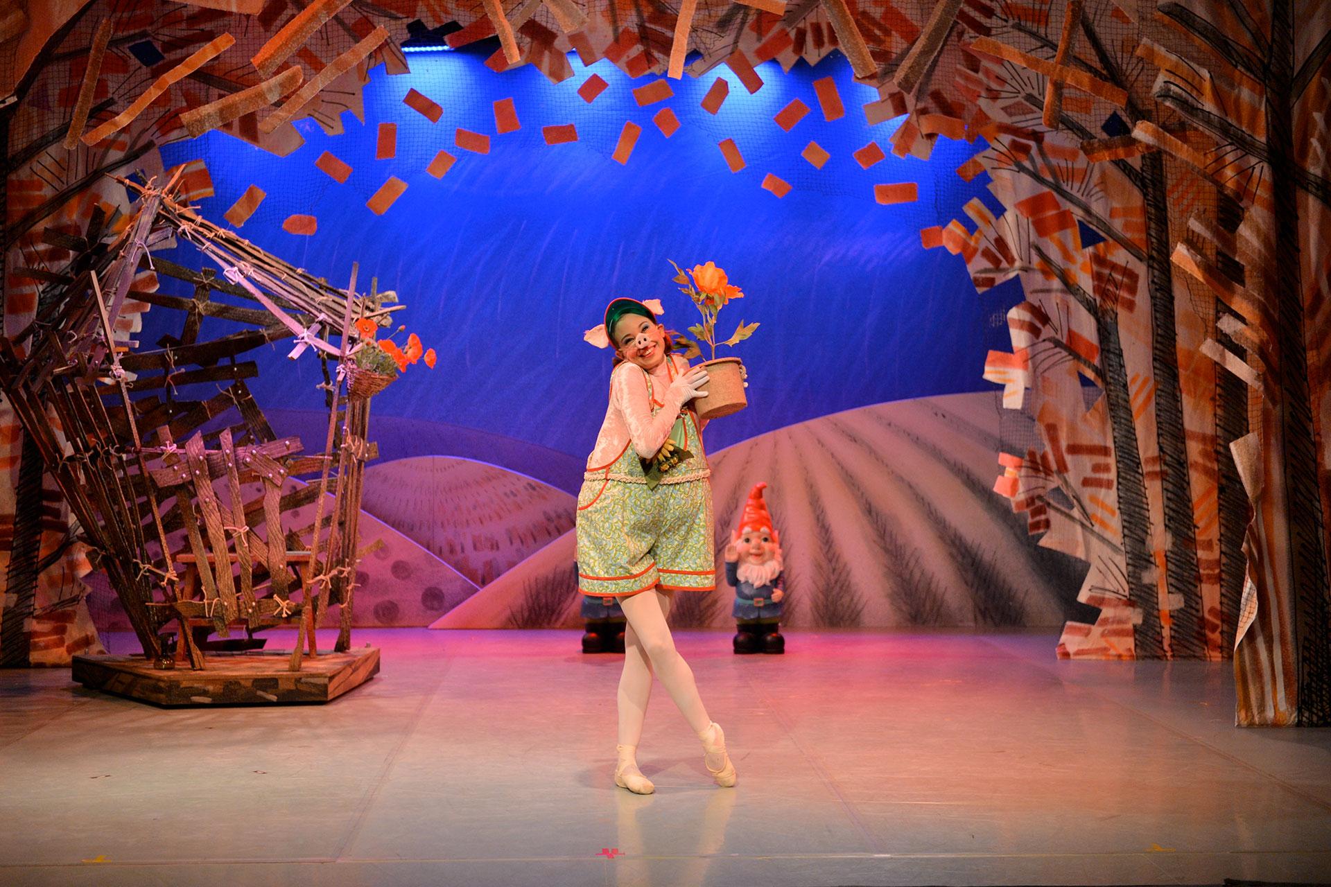 Pig stands proud in front of her house of sticks holding a potted plant