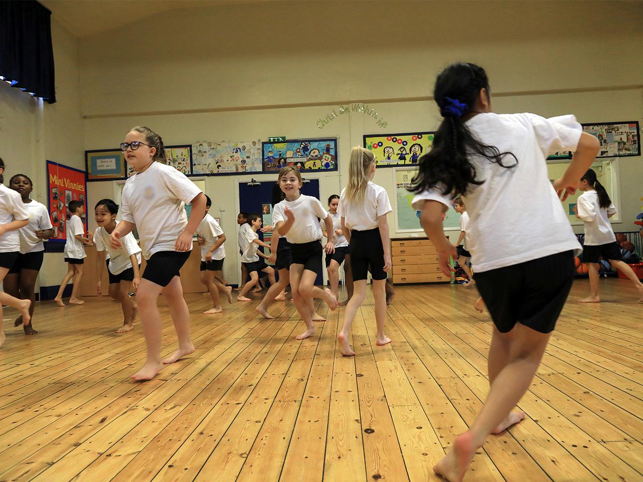 A large group of pupils running around a school hall.