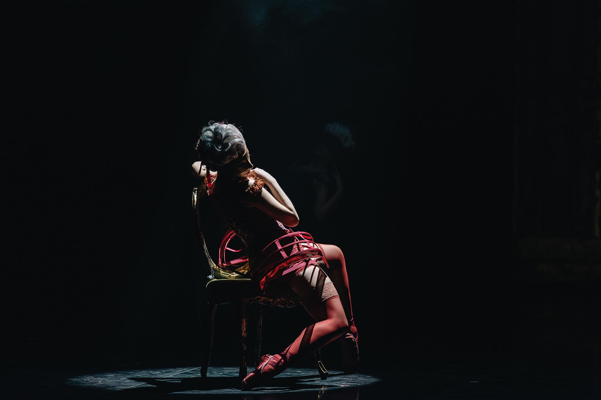 Dancer in red lingerie and red pointe shoes sat on a chair facing away from the camera
