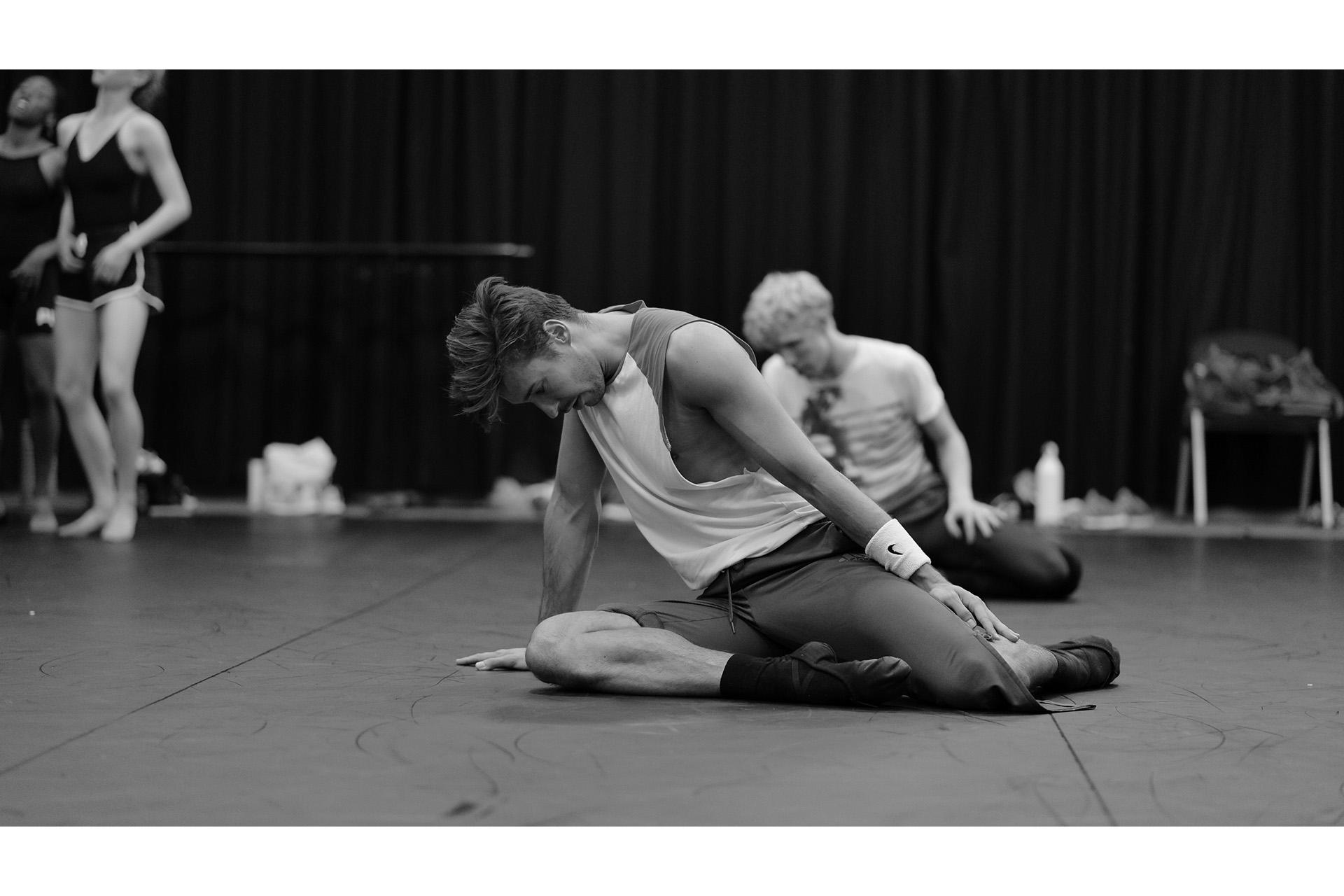 Dancer sits on the studio floor looking dejected at the floor