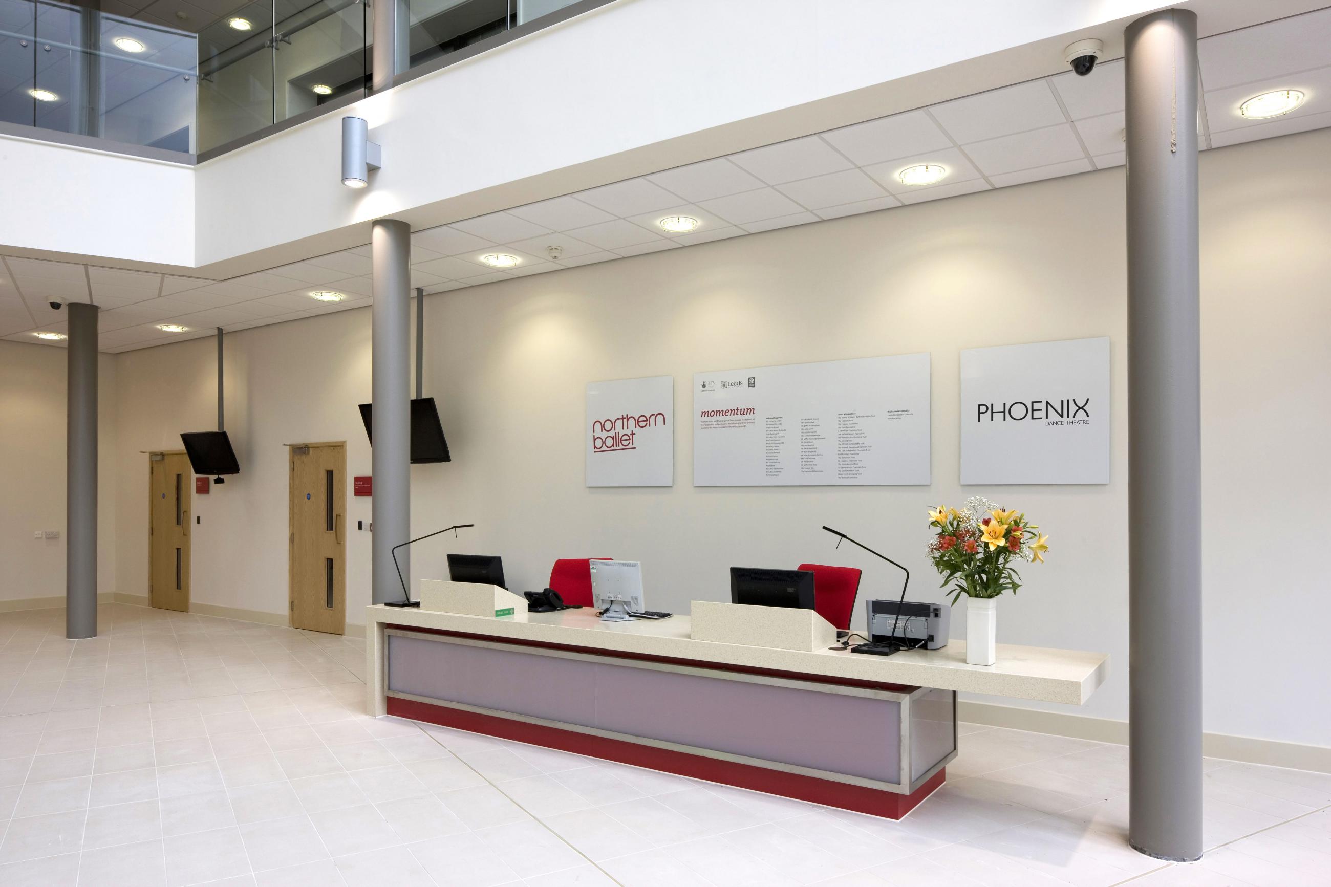 The reception area in Northern Ballet's building. there is a long desk with two computers and chair, behind the desk there are three boards with Northern Ballet's and Phoenix Dance Theatre's logos.