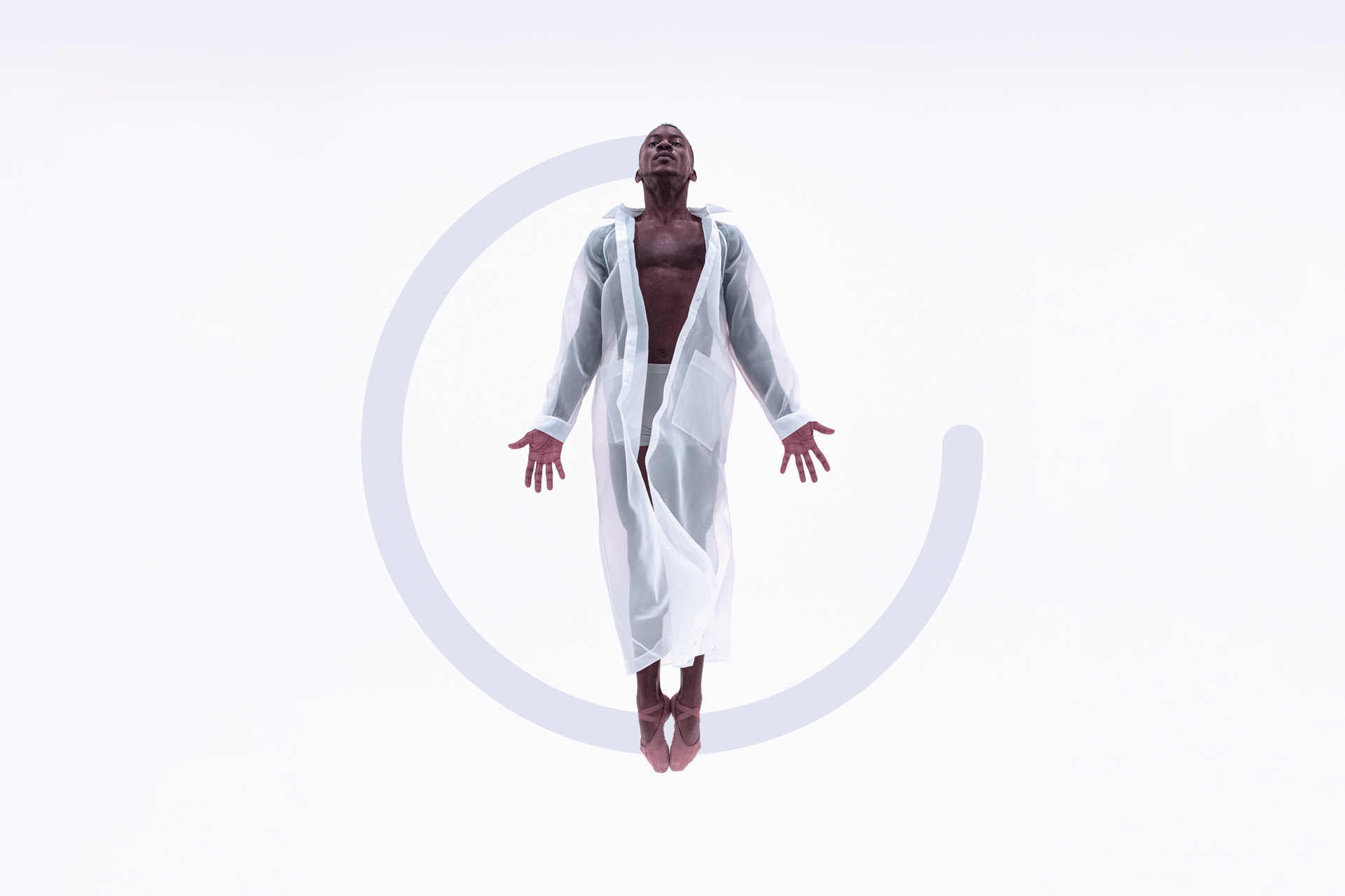 A man is floating in the air wearing a sheer white jacket, which is long sleeve and goes down to their ankles. The are looking up towards the sky with their palms faced to the front. There is a grey semi-cirle graphic added to the image behind the dancer.