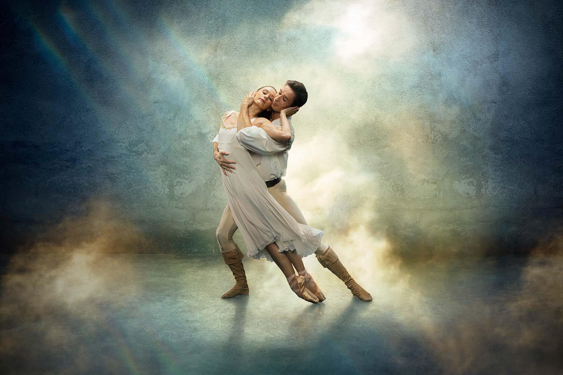 Star-crossed lovers Romeo &amp; Juliet in a loving embrace, both wearing white against a fantasy blue and yellow background.