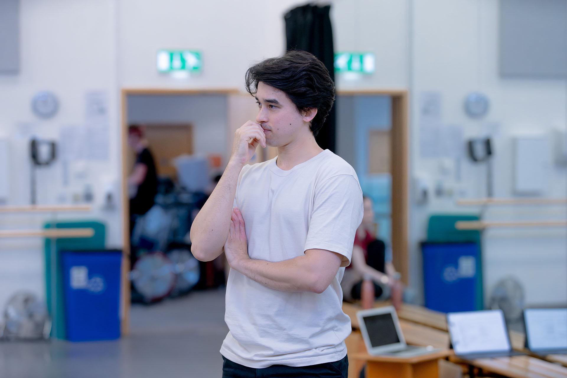 Choreographer standing, one arm folded in front of him, the other with a hand in a thoughtful position in front of his mouth