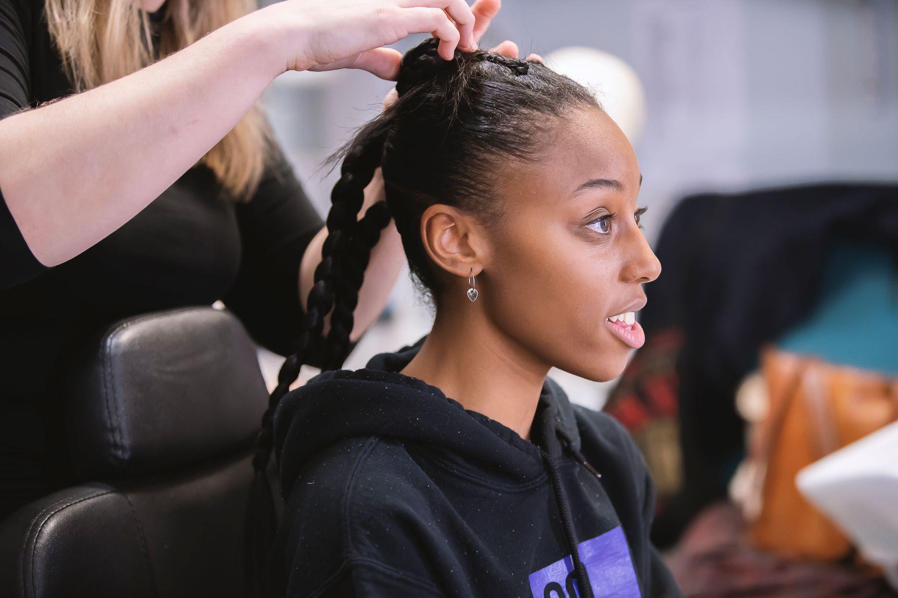 A dancer smiles as a hairstylist adjusts her hair.