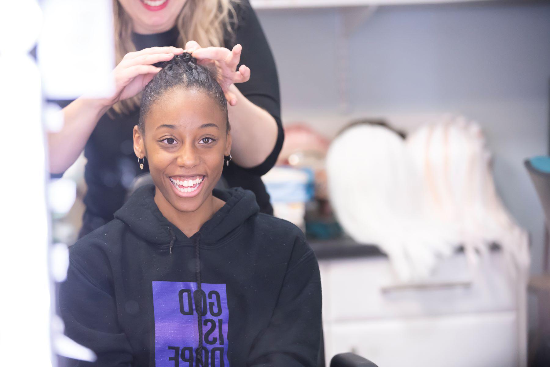 A dancer smiles as a hairstylist adjusts her hair.