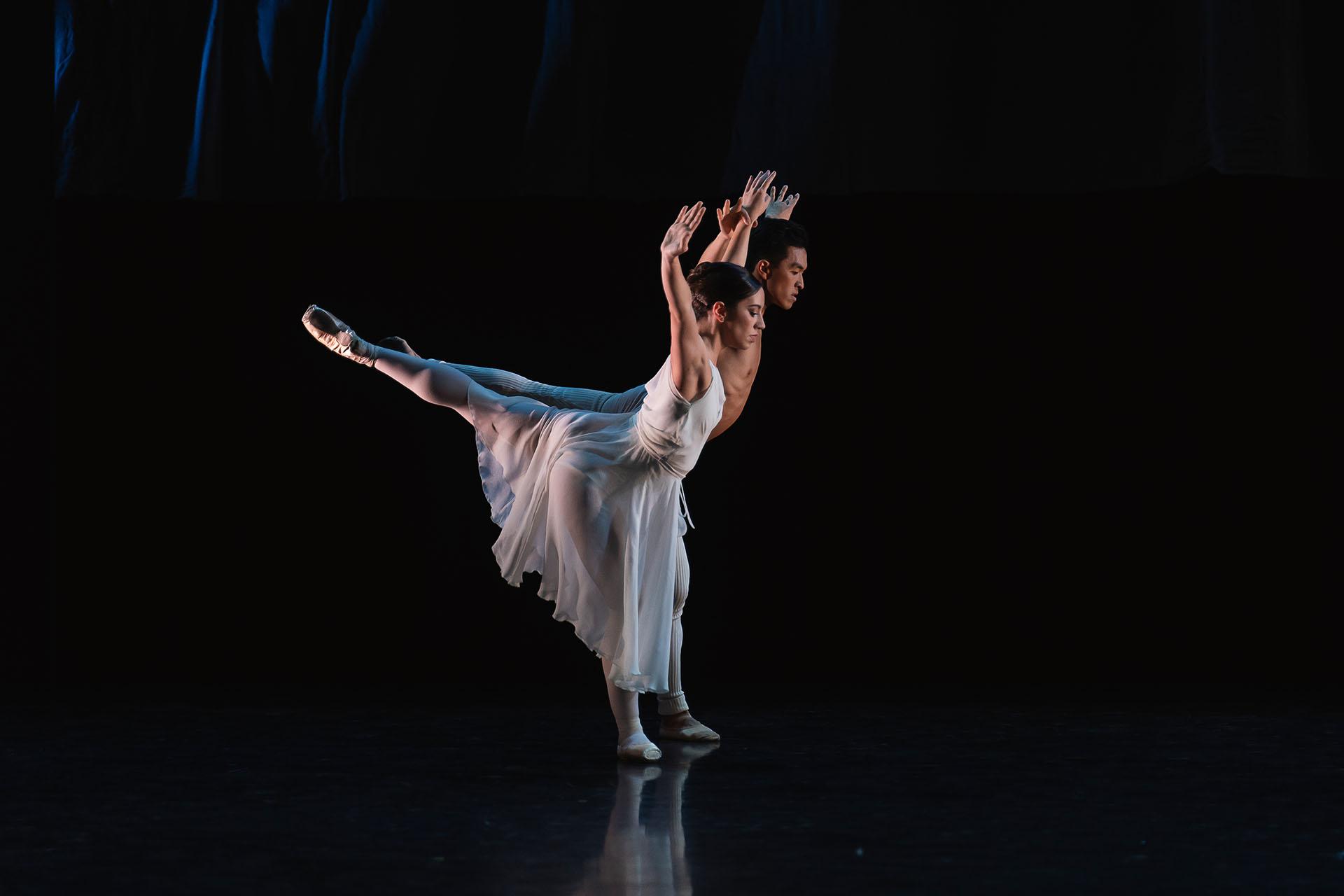 Male and female dancer in white perform synchronous arabesque