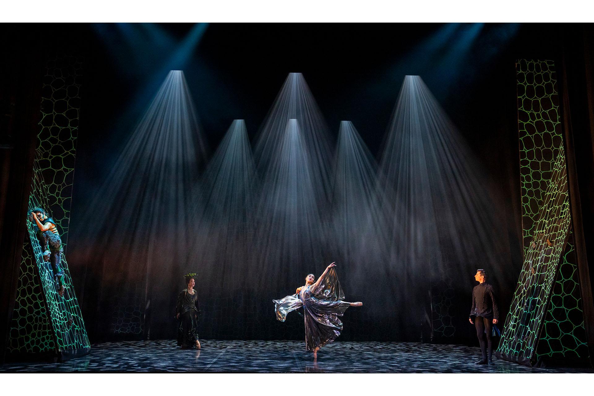 La Fée Luminaire dances centre stage in her silver dress while the butler and La Fée Magnifique watch on