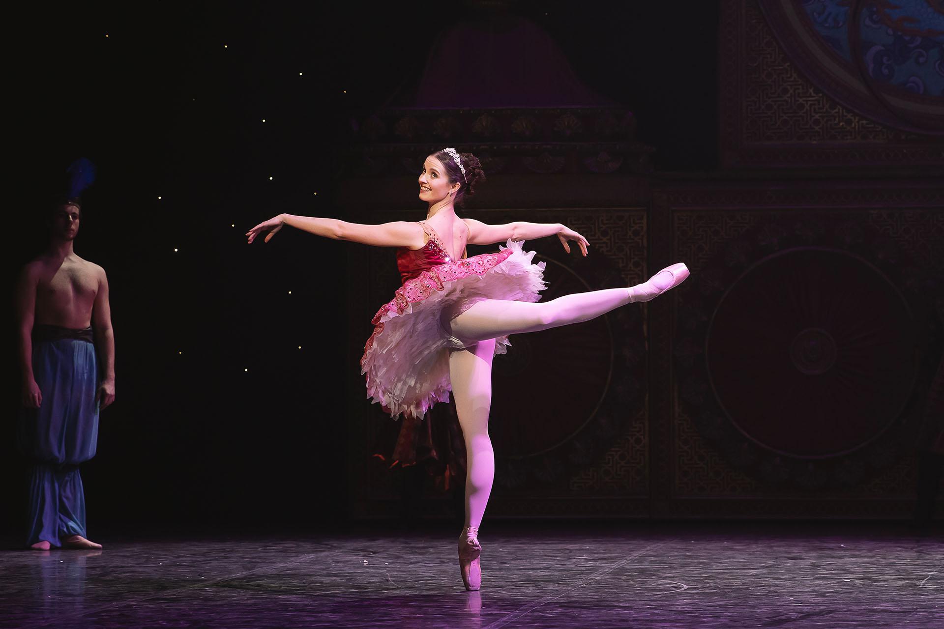 The Sugar Plum Fairy poses en pointe on one leg, her other leg extended behind her, her arms parallel with the ground for balance
