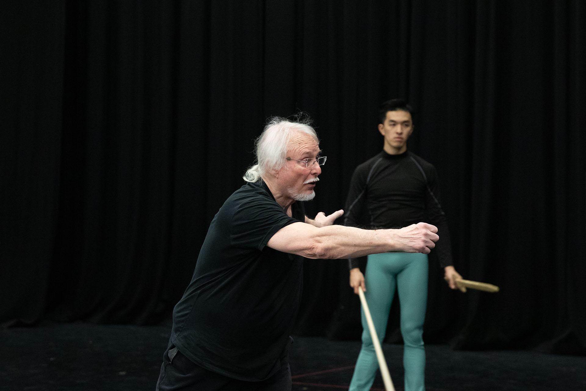 The fight director of Romeo &amp; Juliet in black T-shirt and trousers speaks to people off-camera