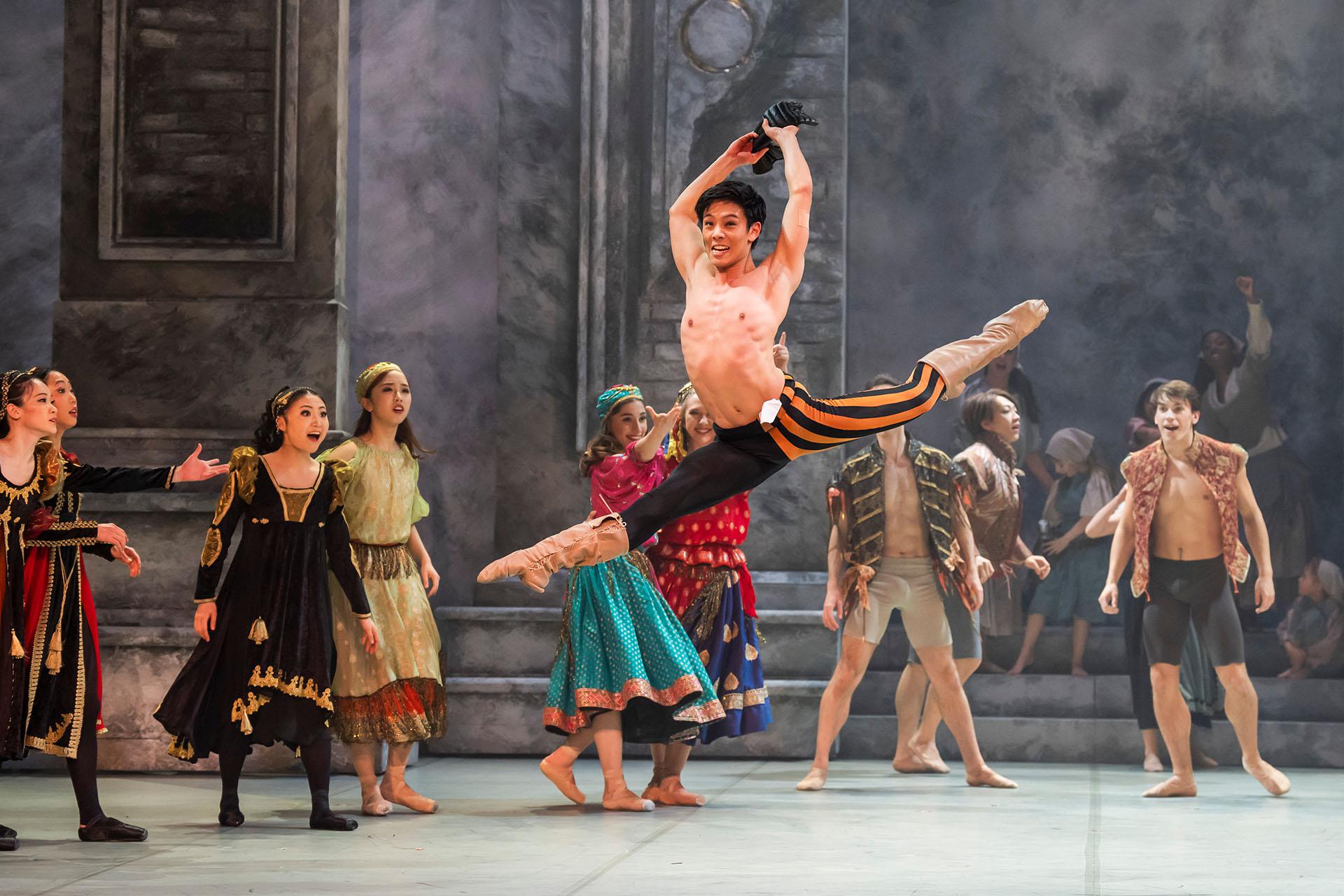 Dancer joyously leaps high above the stage while others look on in wonderment