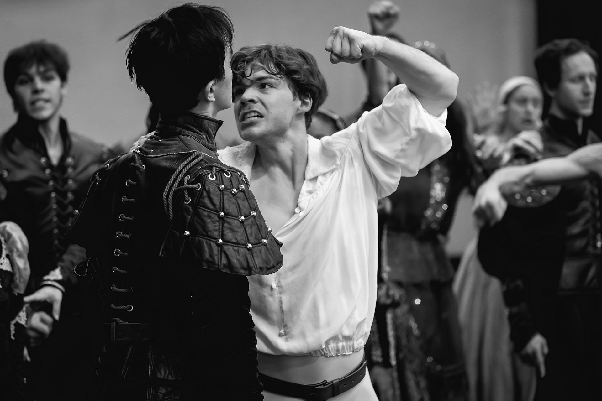 Black and white photo of two people close to fighting, one has a fist raised and is shouting at the other while they are standing implacably before them