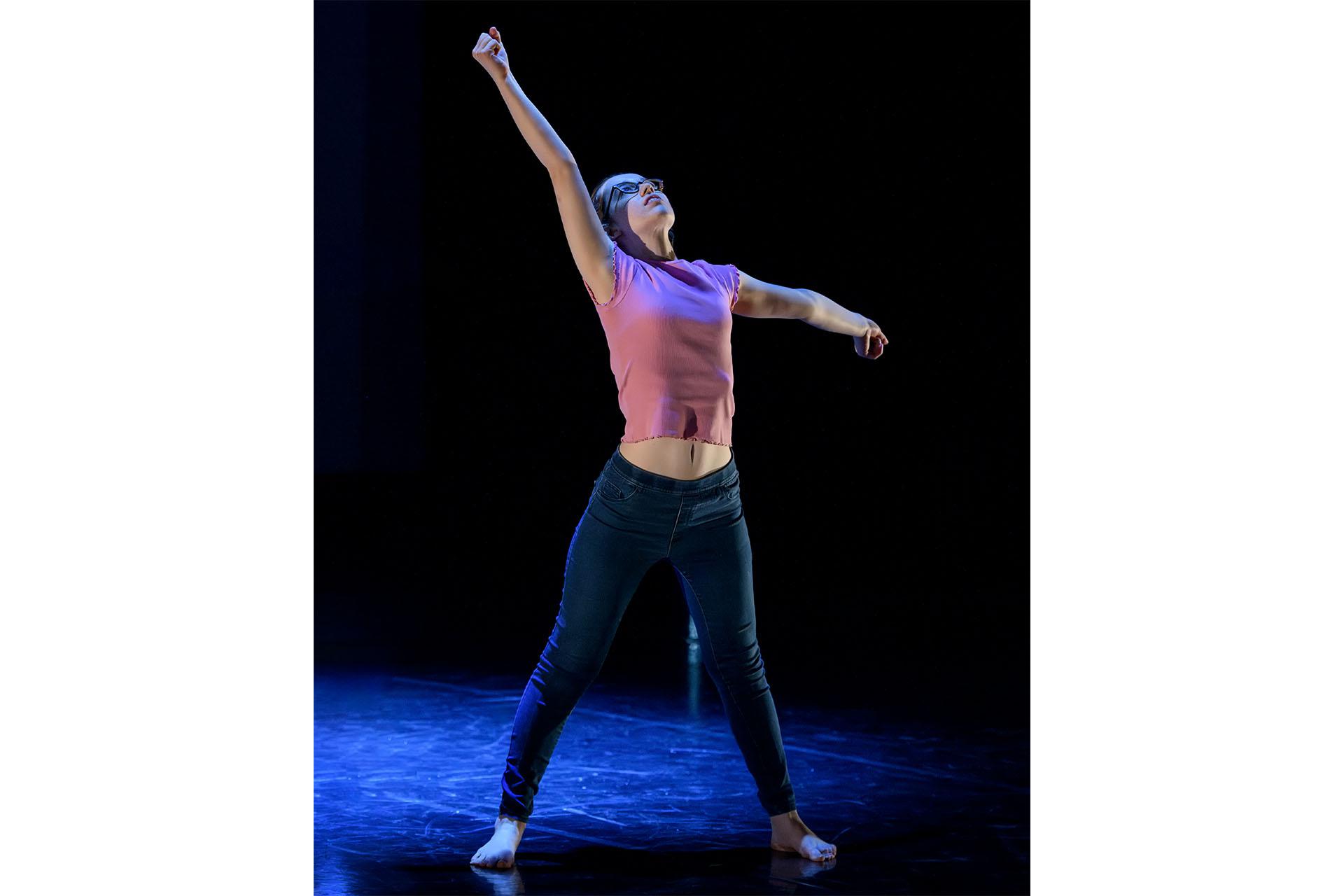 Against a black backdrop a woman stands firmly, her head back and her arms outstretched