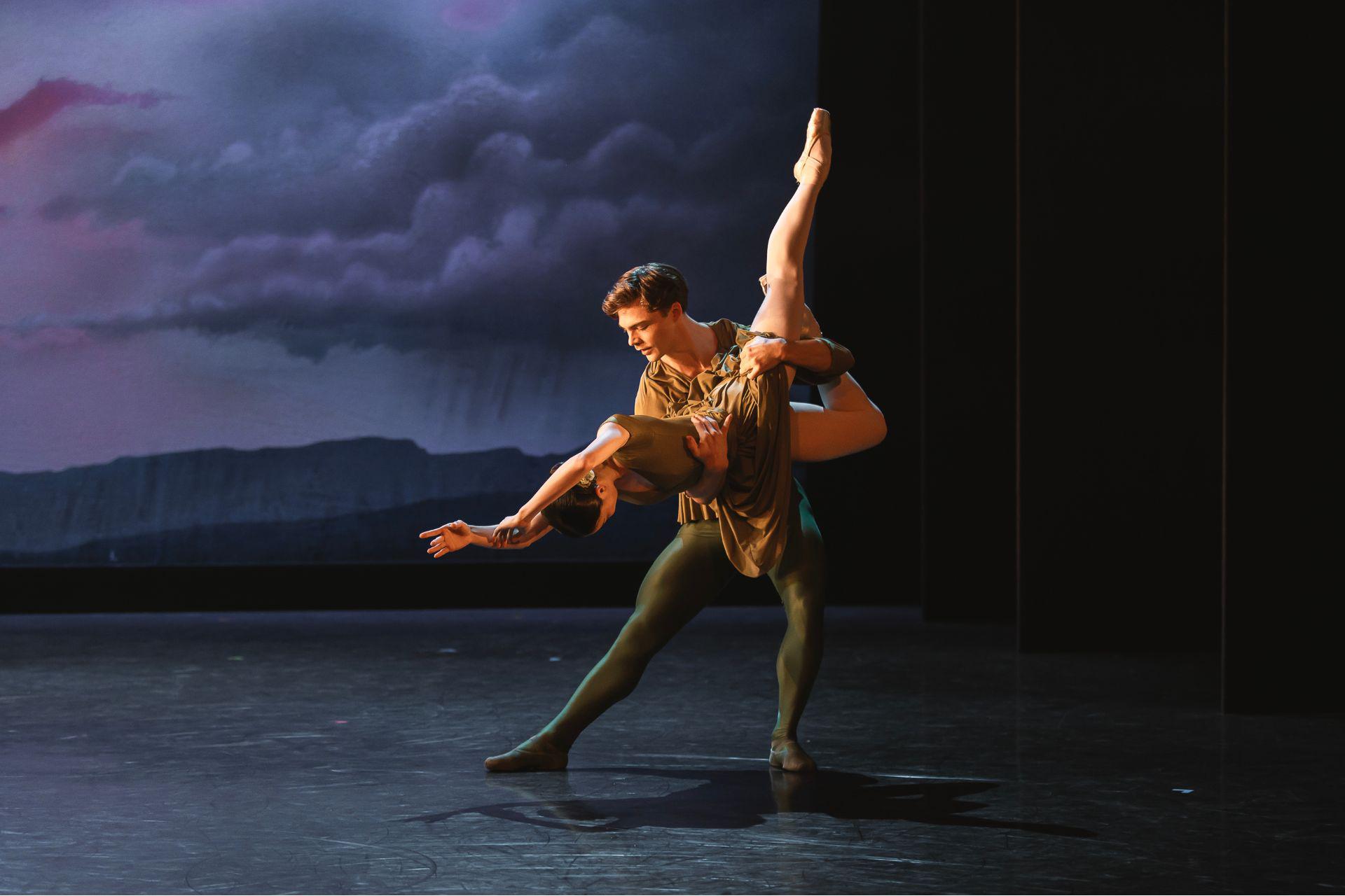 A male dancer lifts a female dancer so that her legs point high in the air and her head and arms point downwards