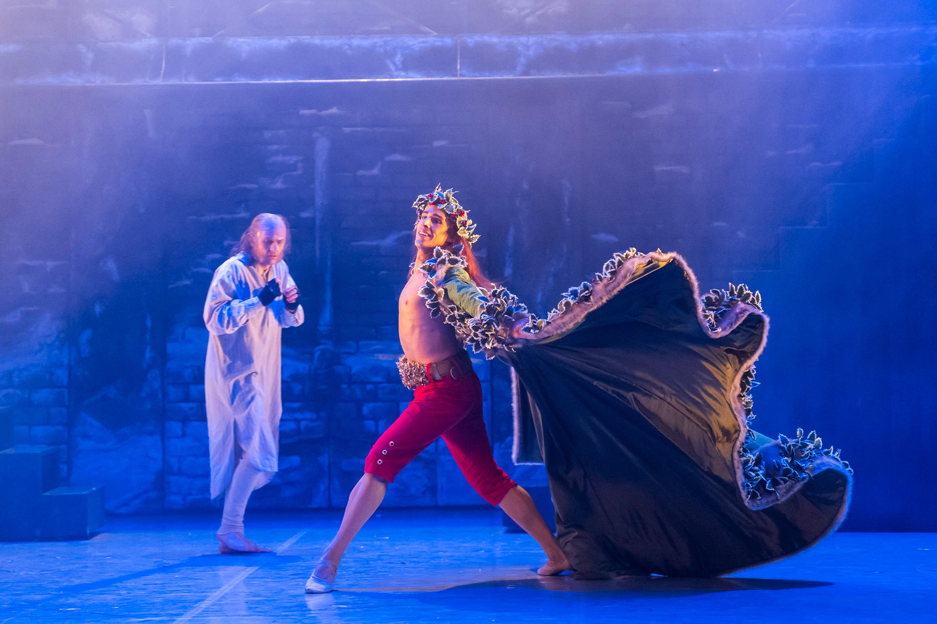 The Ghost of Christmas Present strides past Scrooge, his cape billowing.