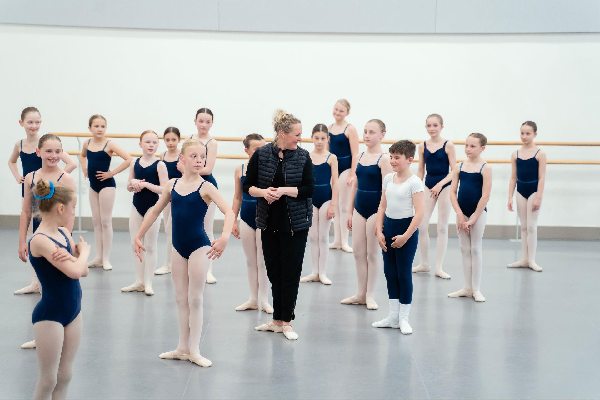 A group of young students stand around a teacher in a ballet studio