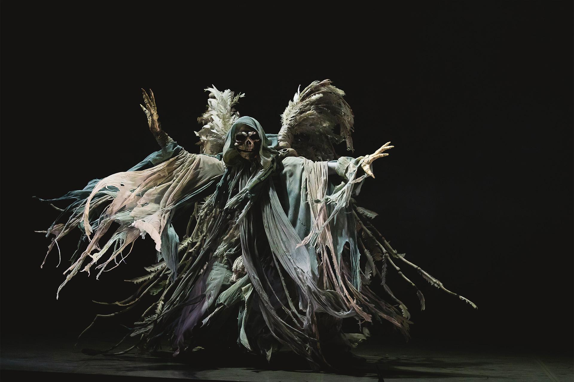 A dancer in a large ghost costume with floating fabric and skull mask
