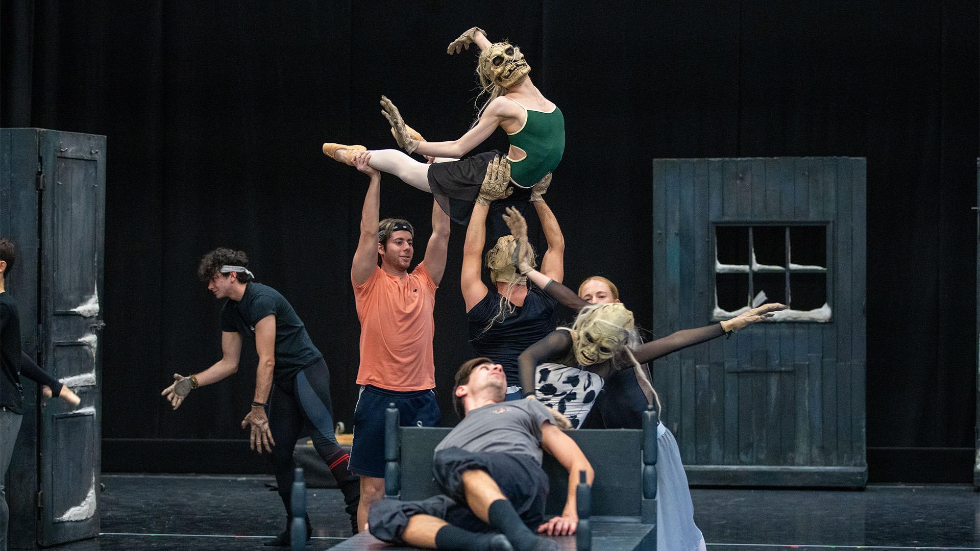 Dancers in phantom masks lifting a dancer while she arches back in a ghostly way.