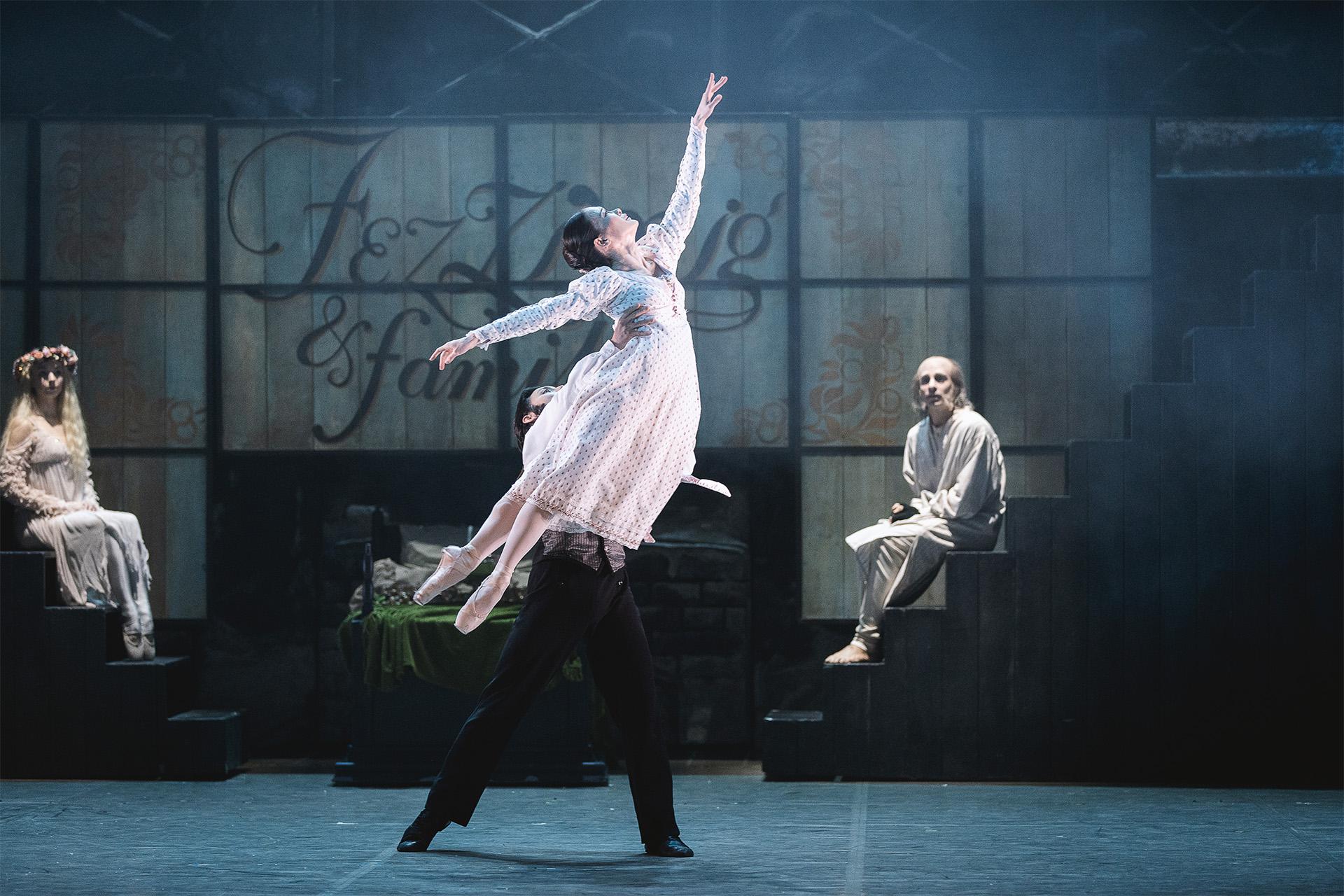 A dancer on stage in a white dress being lifted through the air