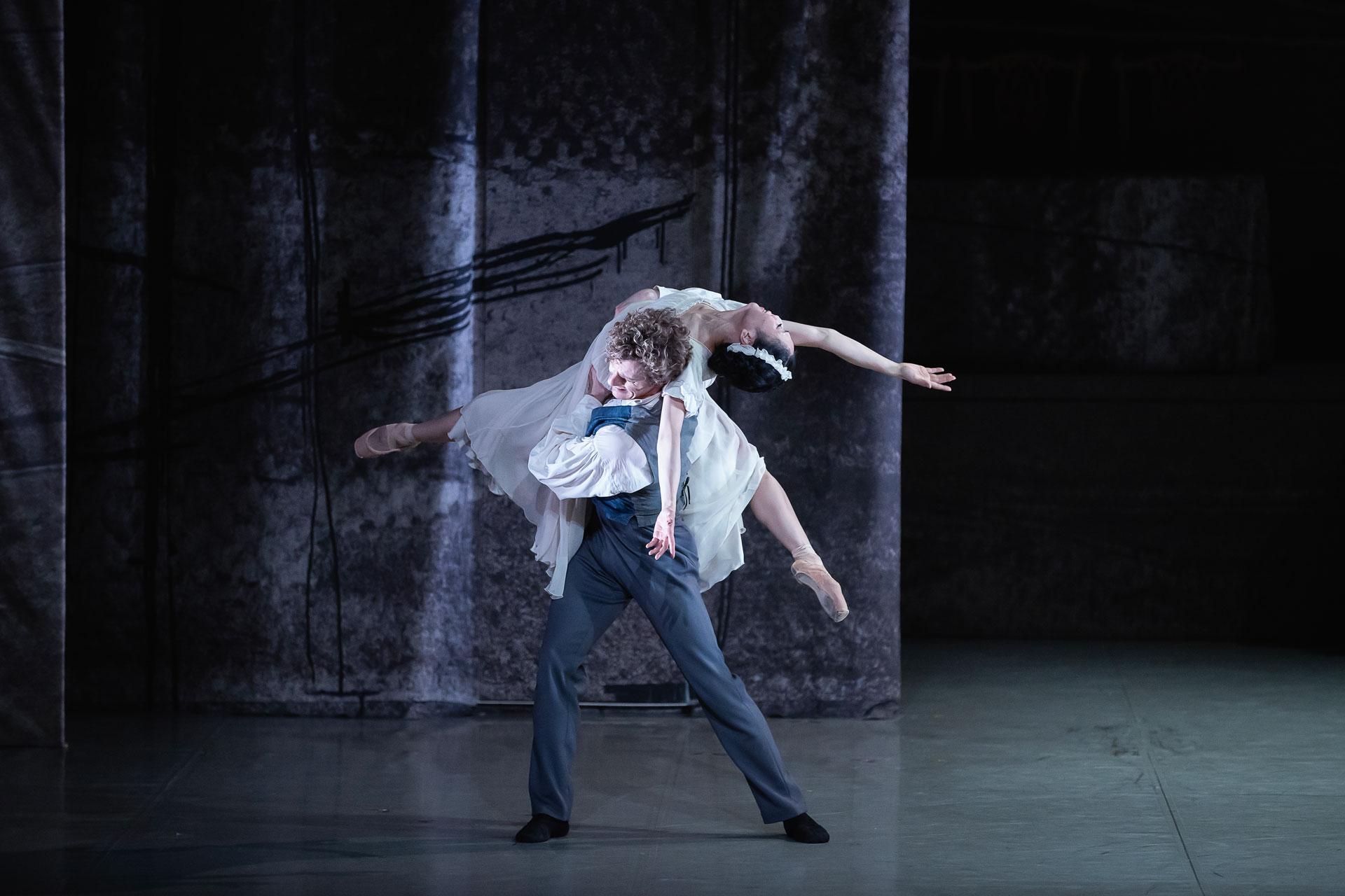 Two dancers in a lift, one draped backwards with arms and legs outstretched while the other dancer lifts her and walks forward.