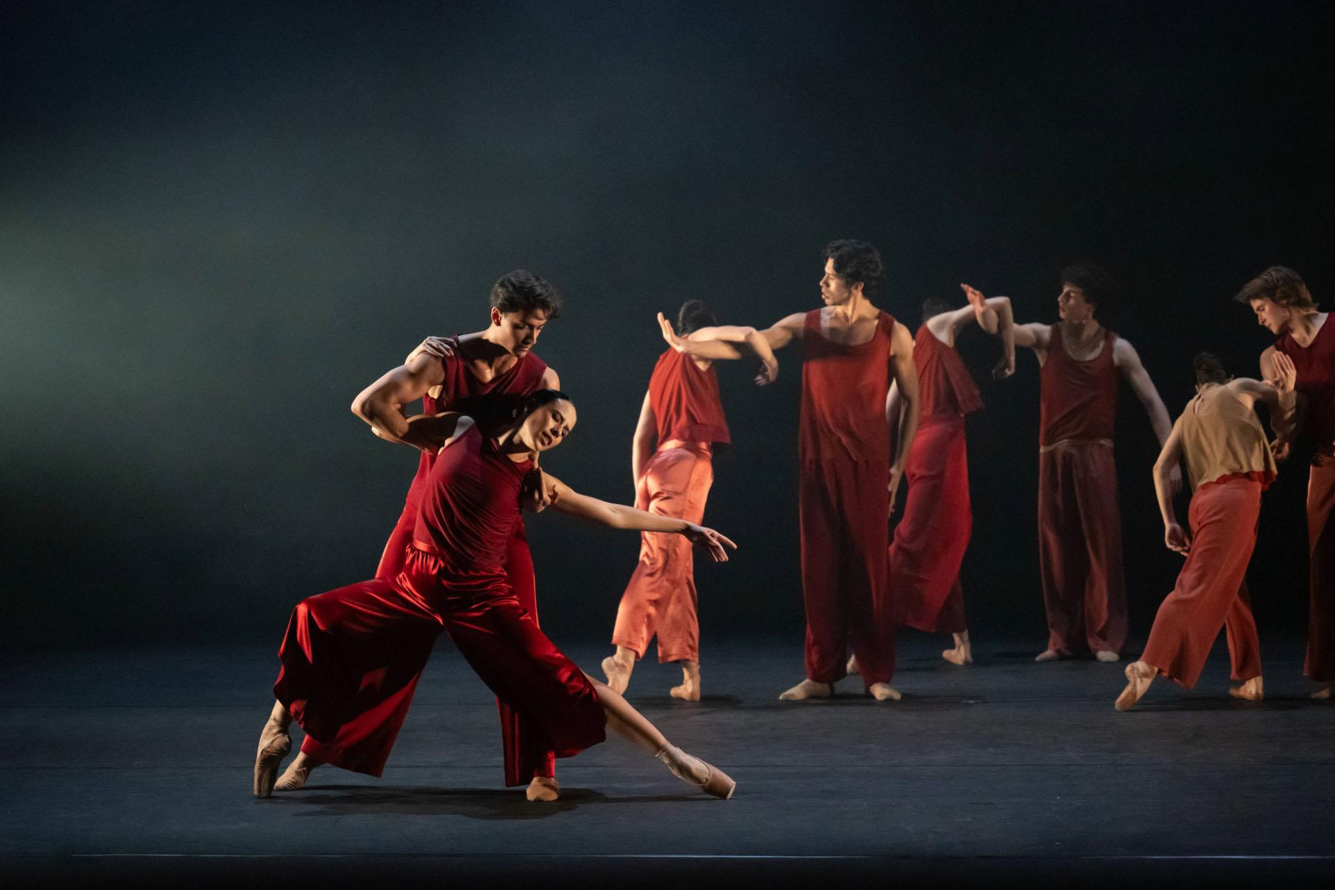 Dressed in red, one dancer holds the other from behind