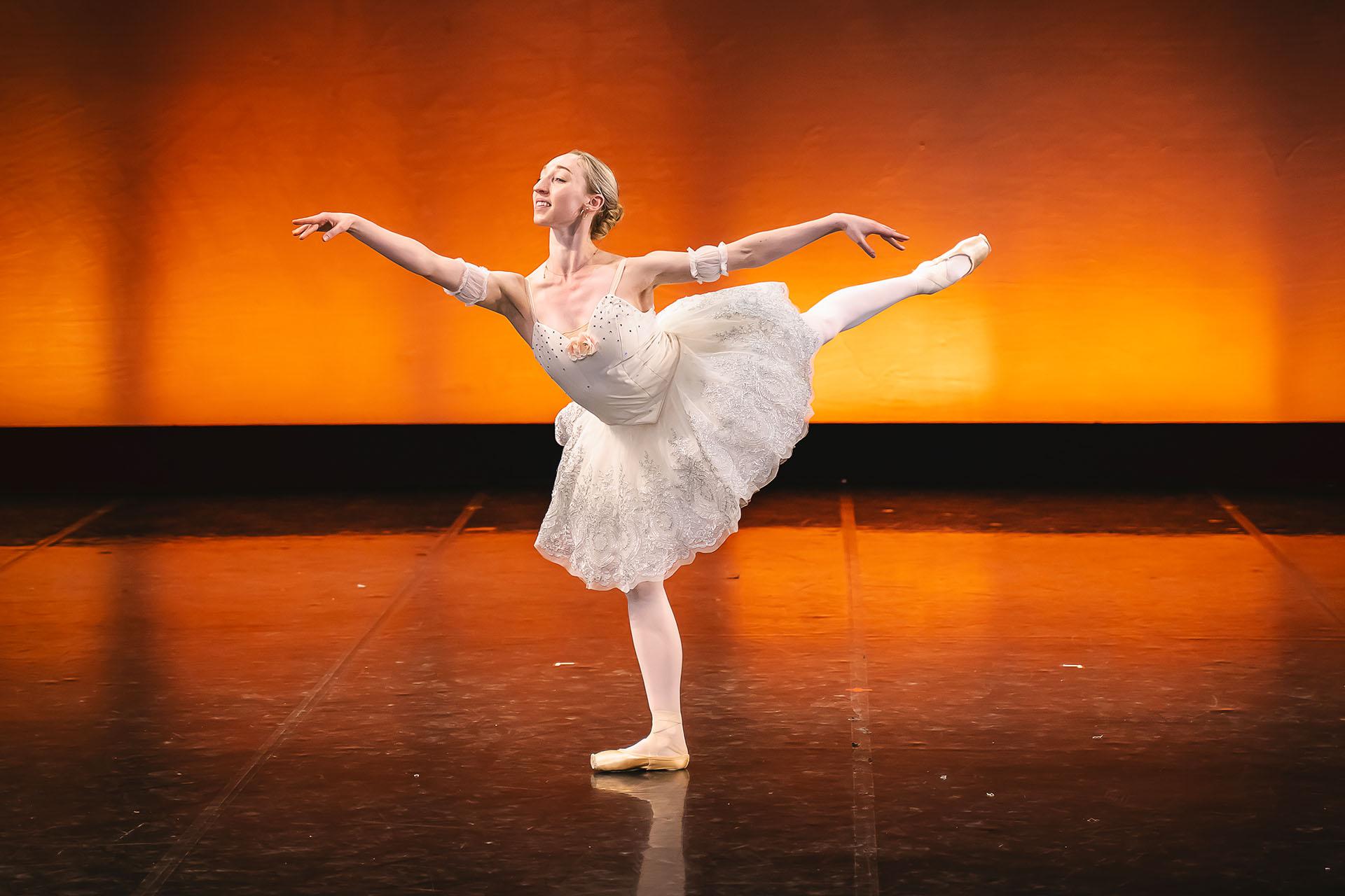 Woman in a white tutu stands arabesque