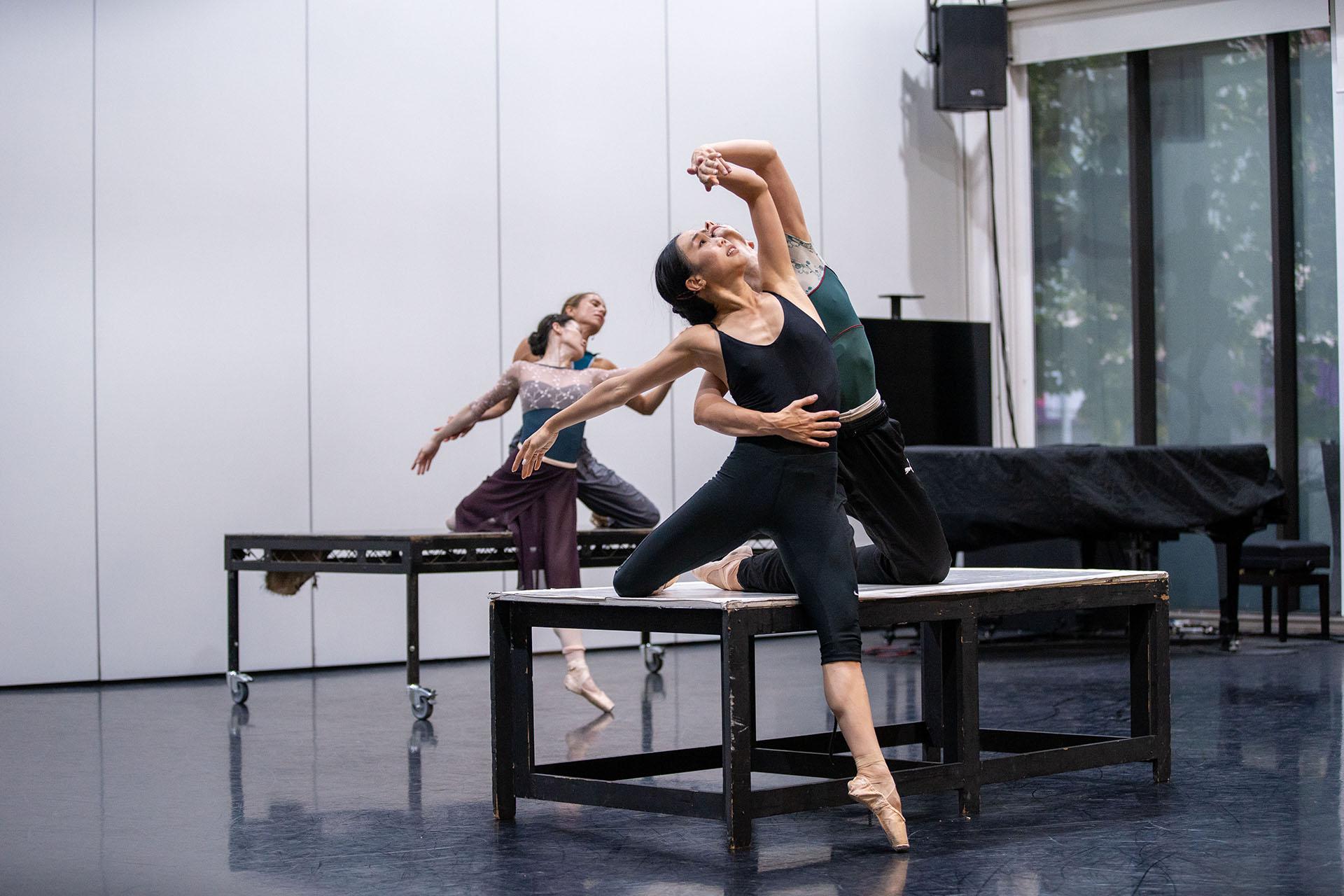 Two dancers on a table, one with a foot on the floor, the other behind her, one arm around her waist, the other lifting her arm above her head