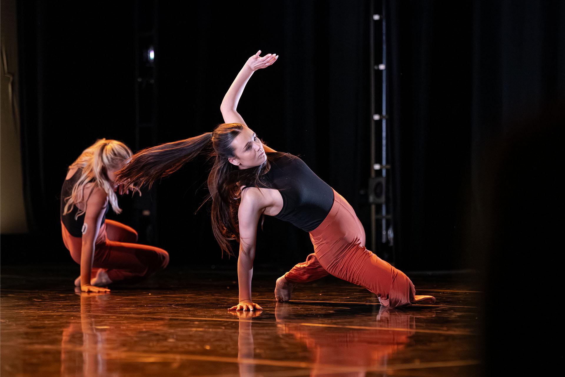 Two people dancing, both feet and one arm on the floor, long hair horizontal with the force of movement, other arm raised purposefully in the air