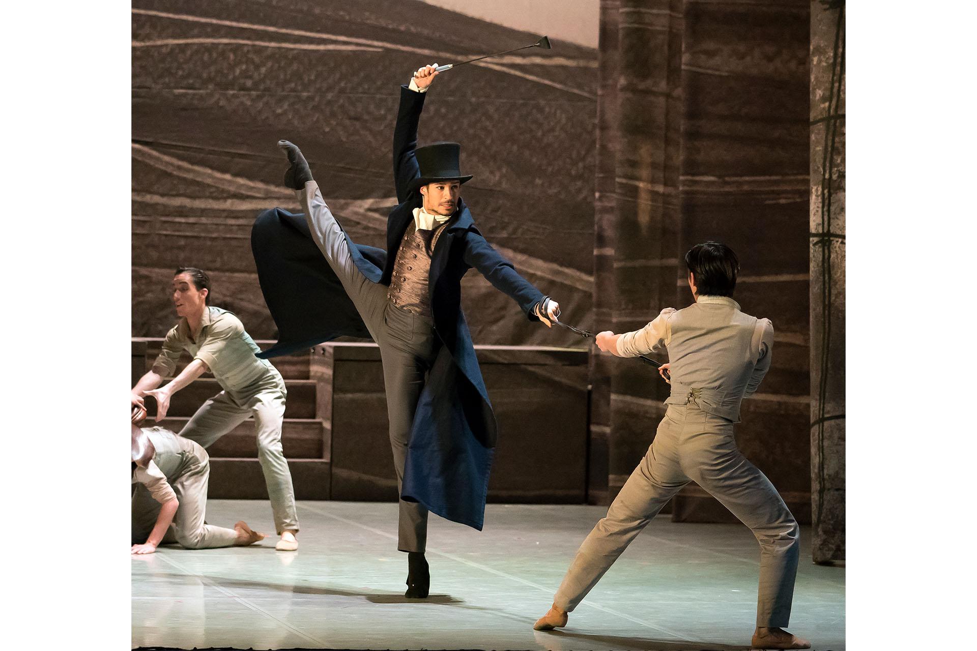 Man in top hat, dark overcoard, fine waistcoat and trousers hold a riding crop above his head, stands firmly on one foots toes, the other leg raised high, mean in grey clothes rush around him nervously.