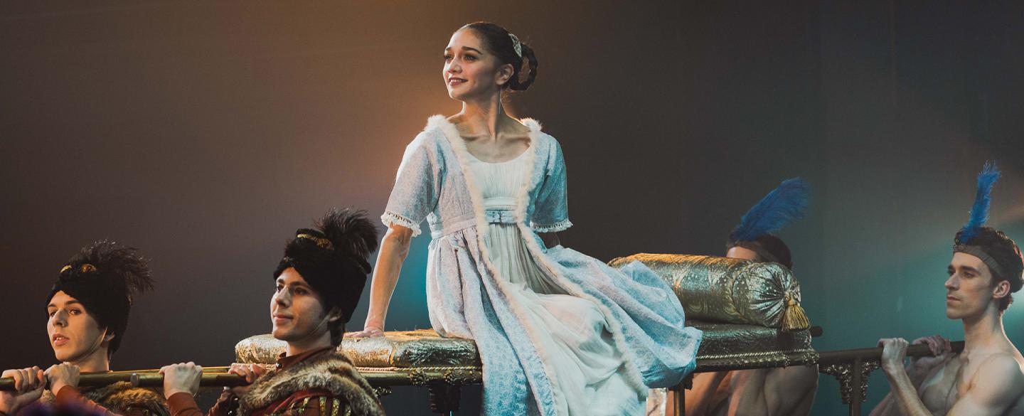 A young woman on a sedan chair held aloft on the shoulders of four dancers