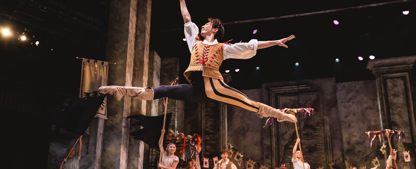 Leaping his above the stage while other cast members look on.