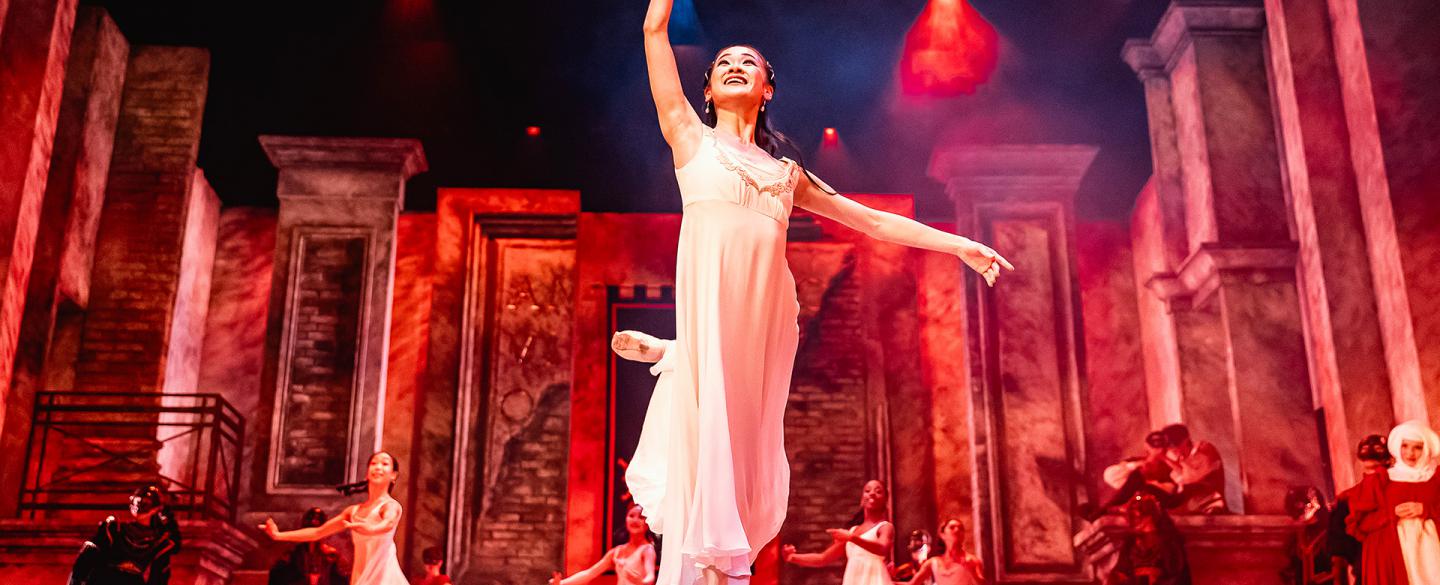 Juliet dressed in a white shift ands en pointe against a dramatically lit set