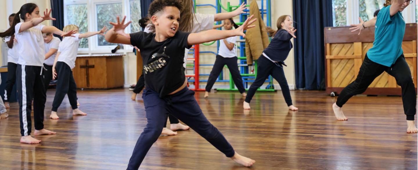 A class of young students stand with legs apart and push forward with open palms.