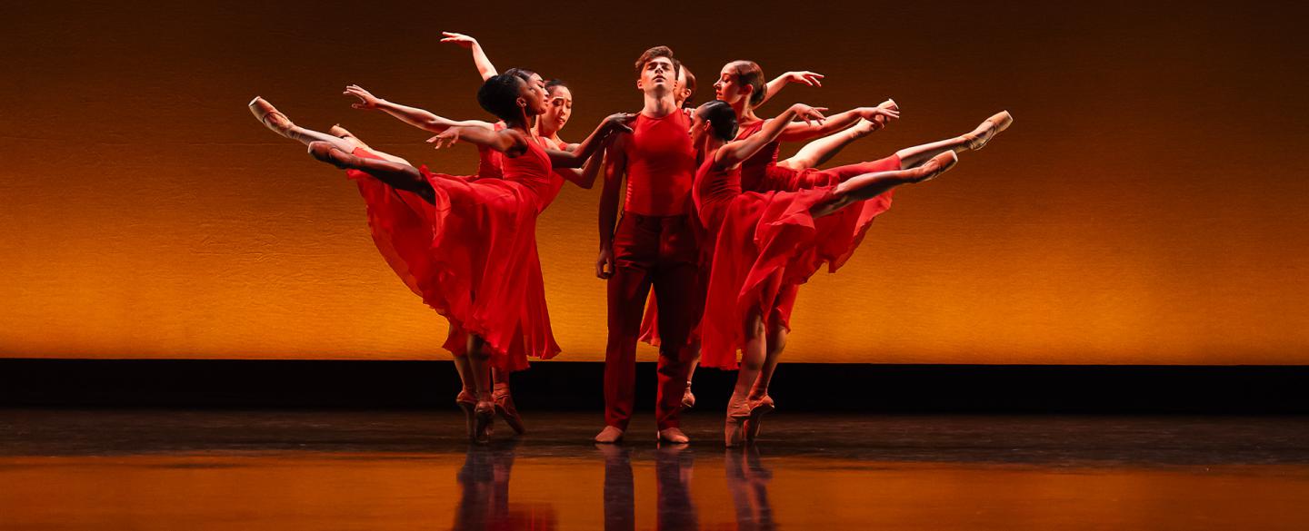 A male dancer stood in the middle of group of dancers in warm red and orange tones