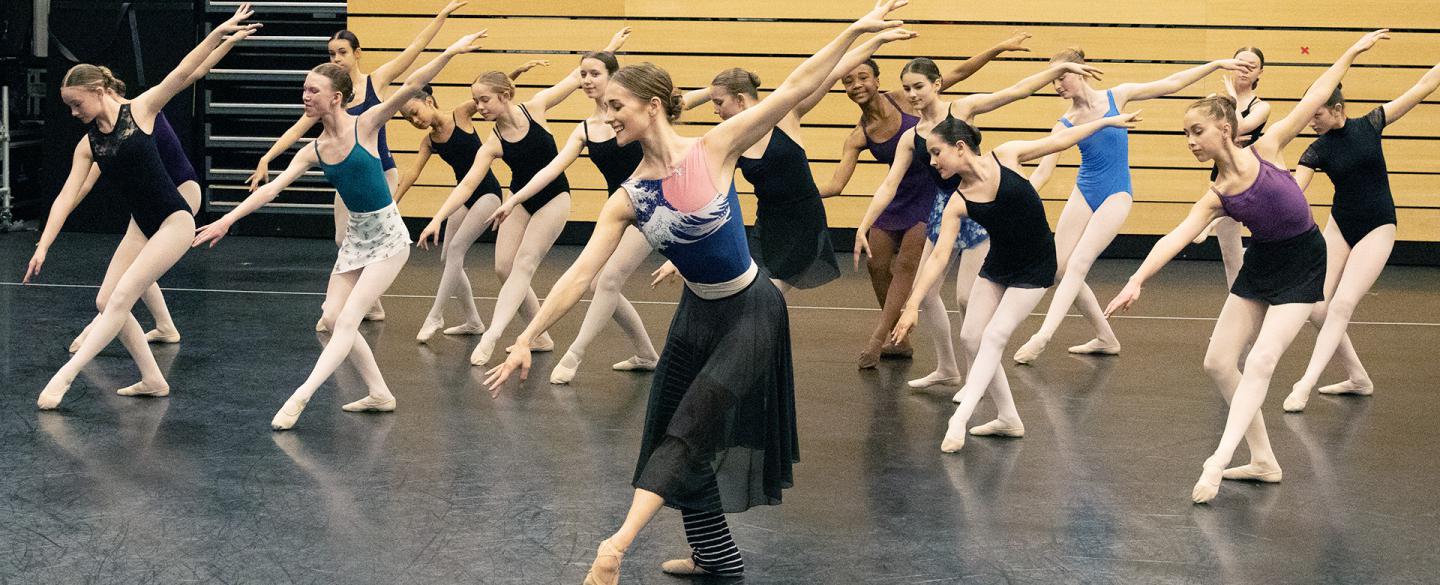 Students copying the ballet pose performed by a dancer in front of them