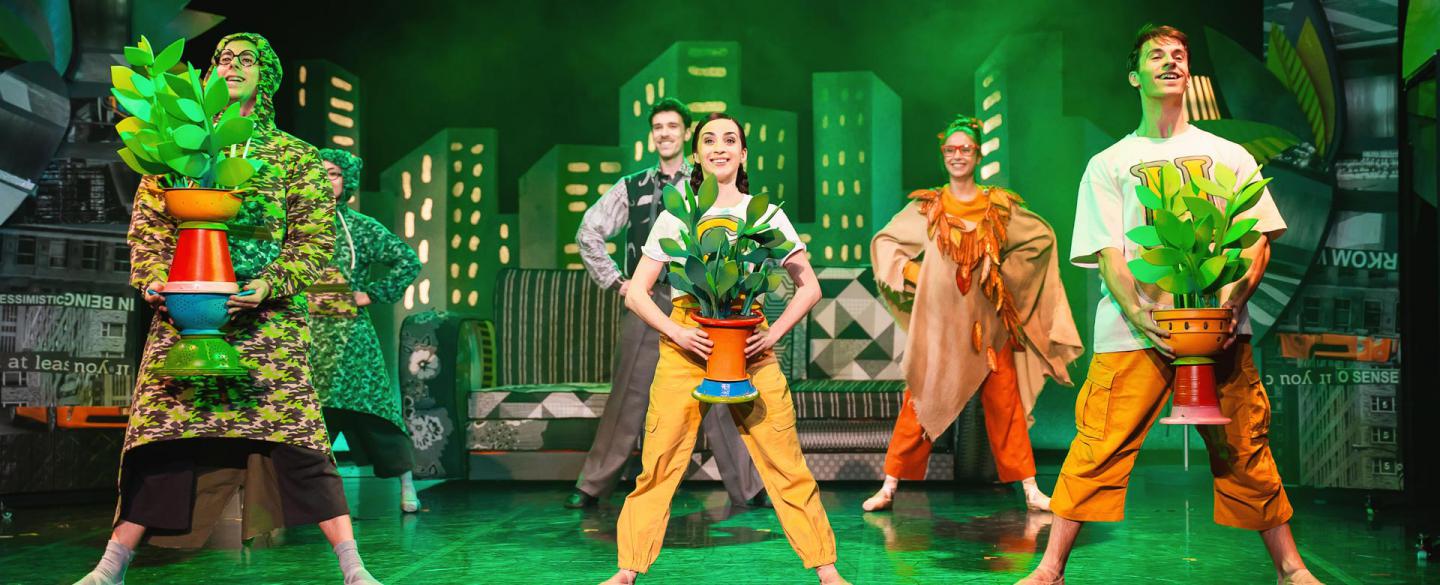 Dancers stood in a row holding potted plants in a soft green light