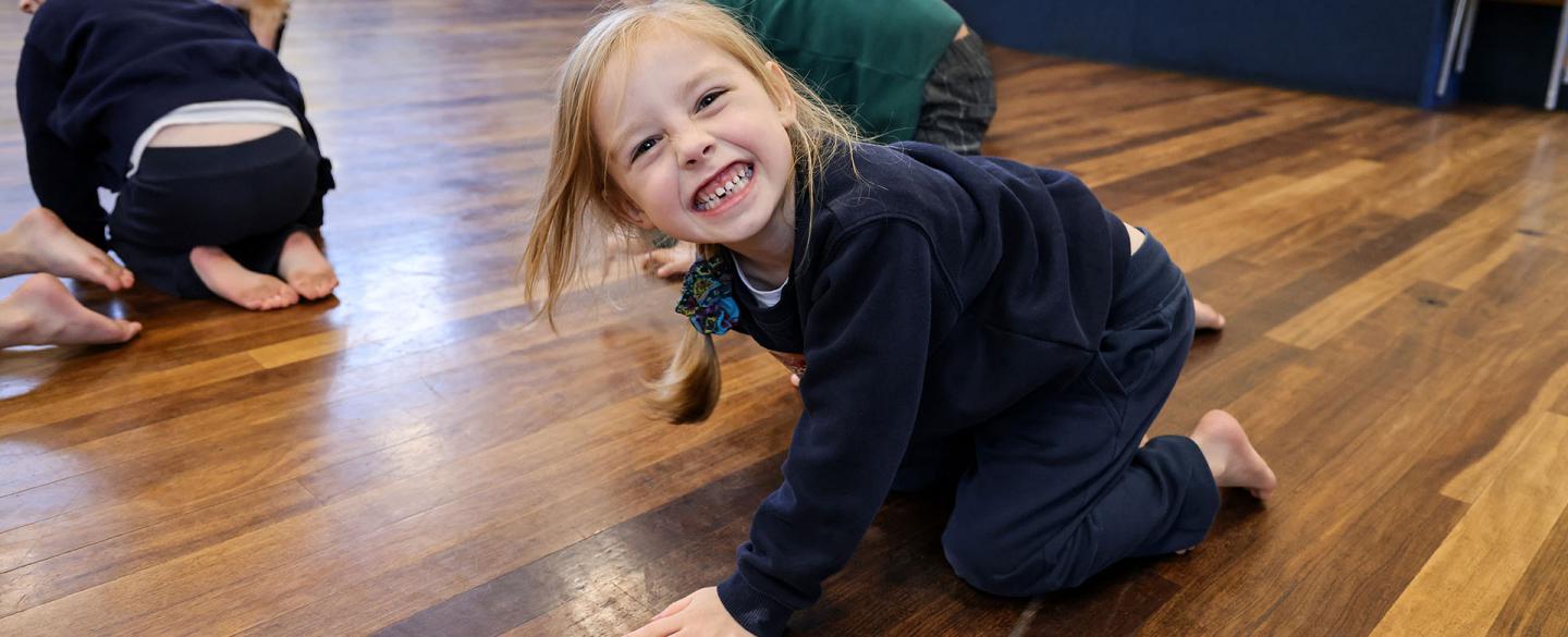 Young student in school hall giving a toothy smile directly at the camera as they stomp on the floor