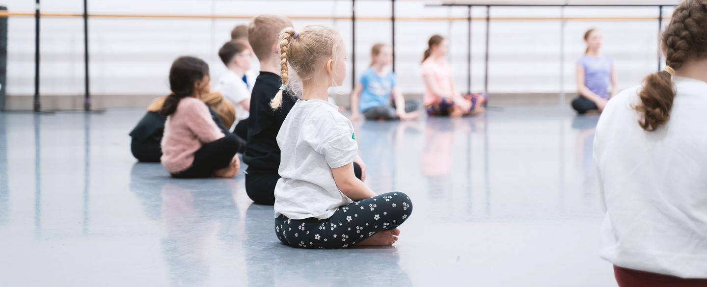 Children sat in a semi-circle cross legged on a dance floor