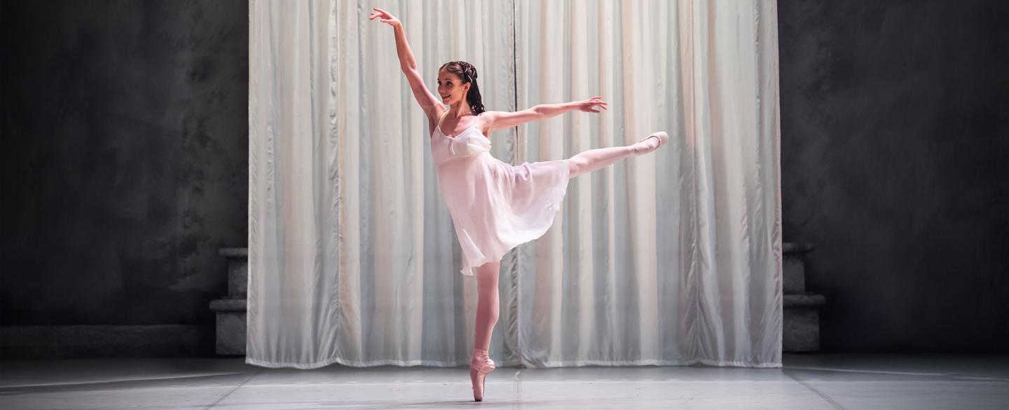 Dancer in white shift standing arabesque en pointe