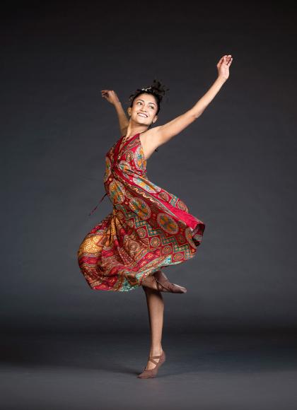 Woman in red patterned dress spinning on one foot with her arms raised joyously.