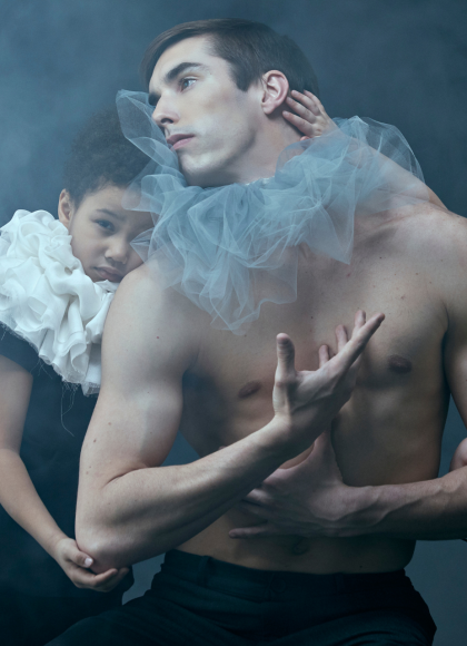 A man and two young children wearing colourful toule around their necks. They are surrounded by smoke with a dark grey background behind them.
