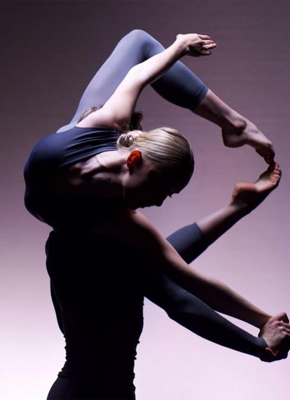 Against a lilac-coloured backdrop one dancer lifts another on his shoulders