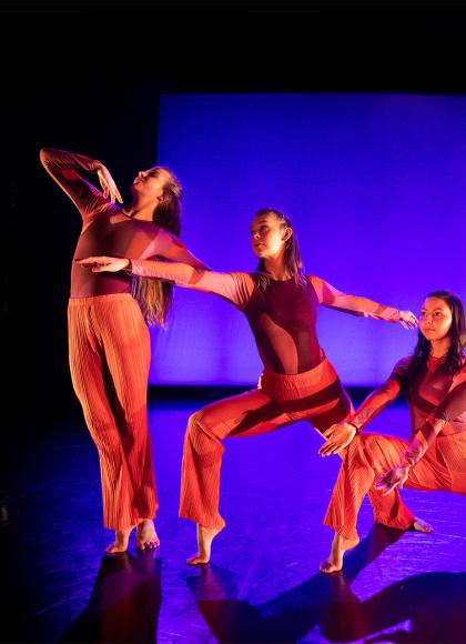 Phoenix Dance Theatre Youth Academy dancers bathed in red light each in a different pose against a blue-lit backdrop