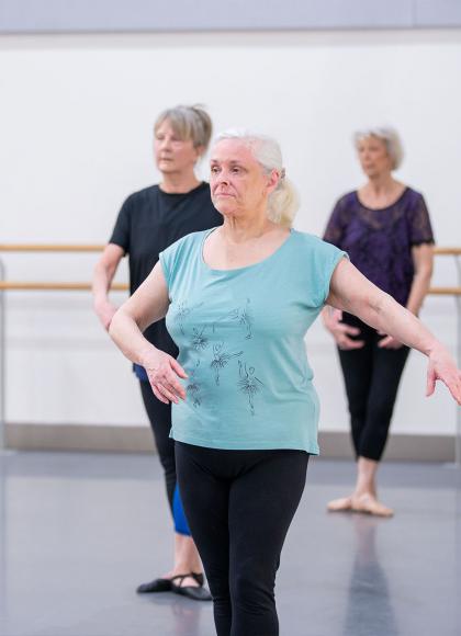 Silver-haired lady in turquoise T-shirt taking ballet class
