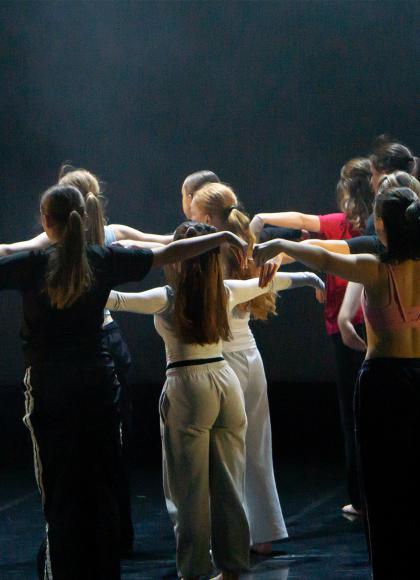 Troop of dancers turned away from the viewer, each standing with their arms straight out level with their shoulders