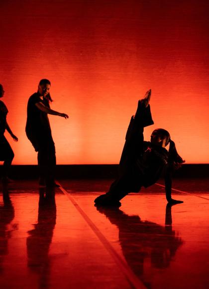 The back is illuminated in red and orange, dancers are closer to us in near silhouette, each in a different but striking pose
